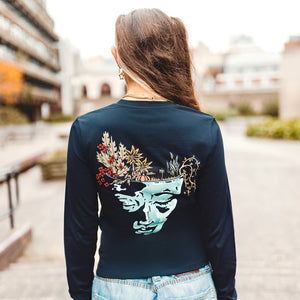 h clothing - female model with back to camera wearing black long sleeved tshirt with graphic of a face and a garden on top of the head