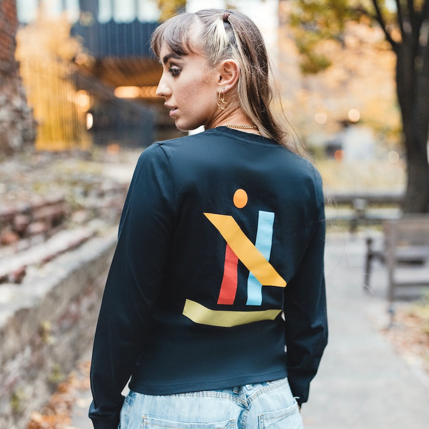 h clothing - female model with back to camera wearing black long sleeved tshirt with graphic of colourful geometric shapes