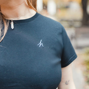 h clothing - close up of female model wearing black tshirt with blue h logo on left breast