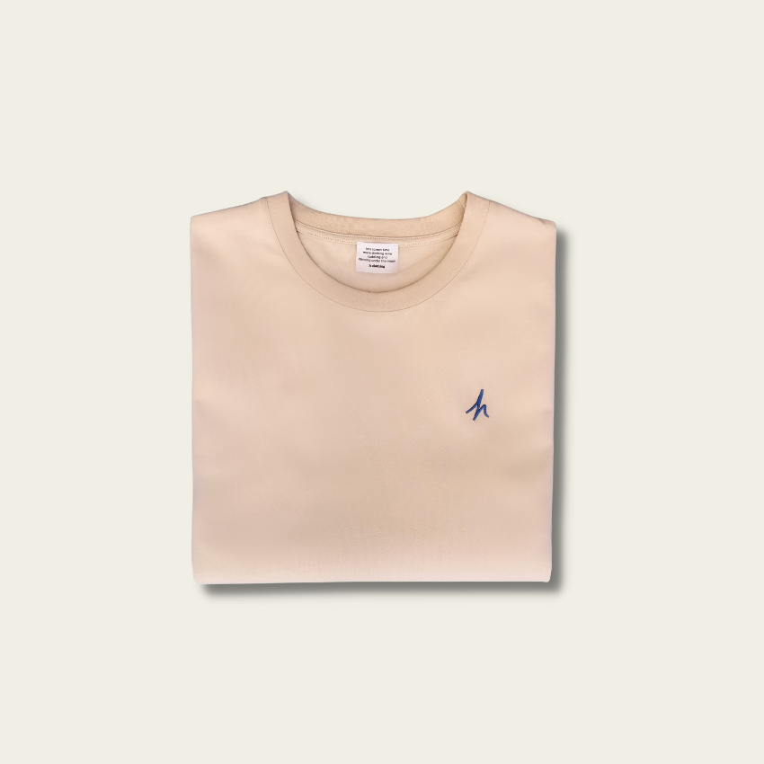 h clothing - flat shot of front of folded sandy tanned tshirt with blue h logo on left breast