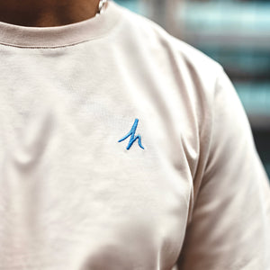 h clothing - close up of male model wearing sandy tanned tshirt with blue h logo