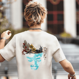 h clothing - male model with back to camera wearing sandy tanned tshirt with graphic of face and garden design