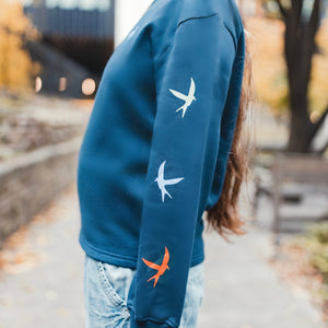 h clothing - close up of female model standing side on wearing navy blue sweatshirt with 3 colourful birds on left arm