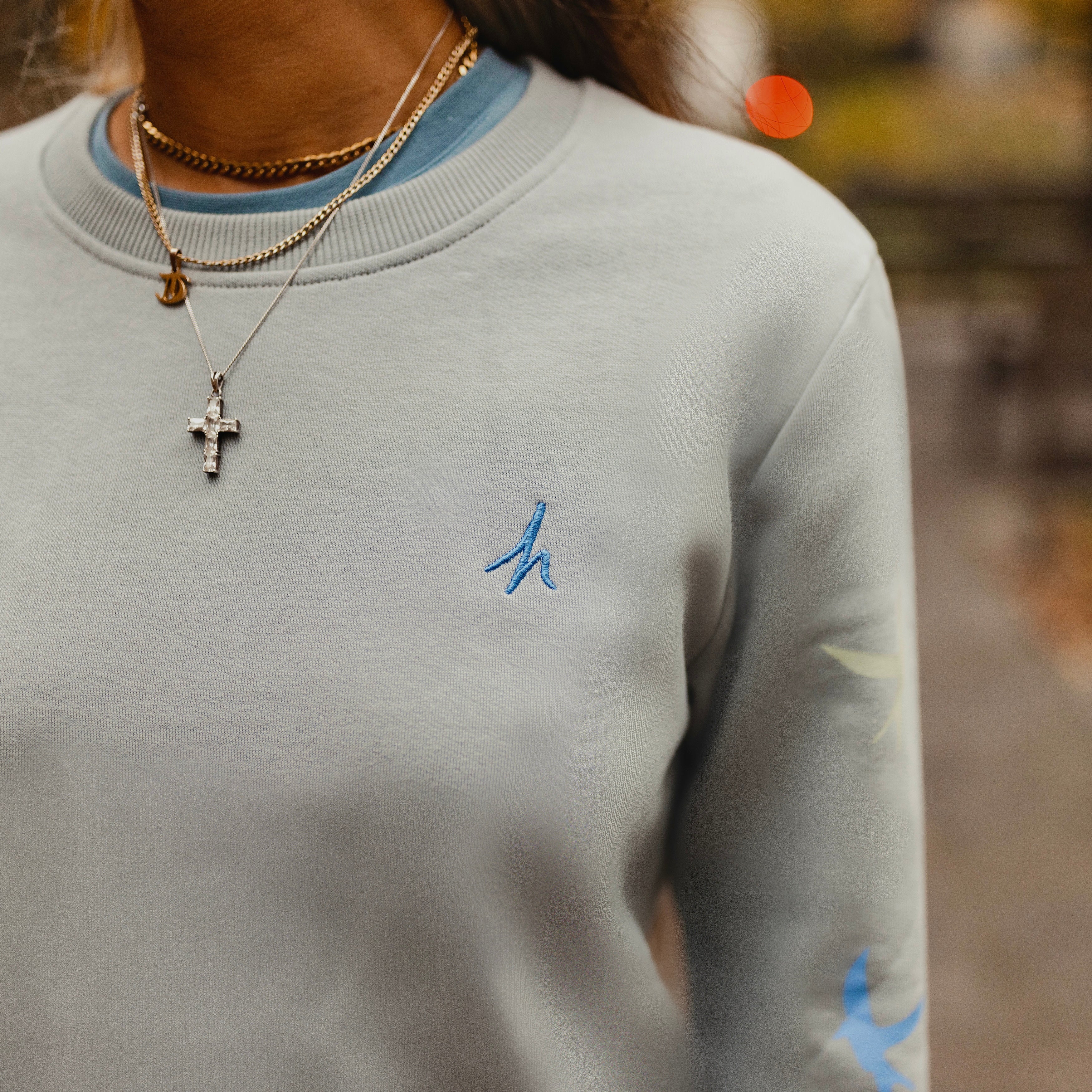 h clothing - close up of female model wearing heather grey sweatshirt with blue h logo on left breast