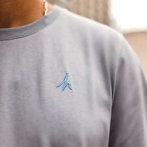 h clothing - close up of male model wearing a pastel grey tshirt with blue h logo on left breast