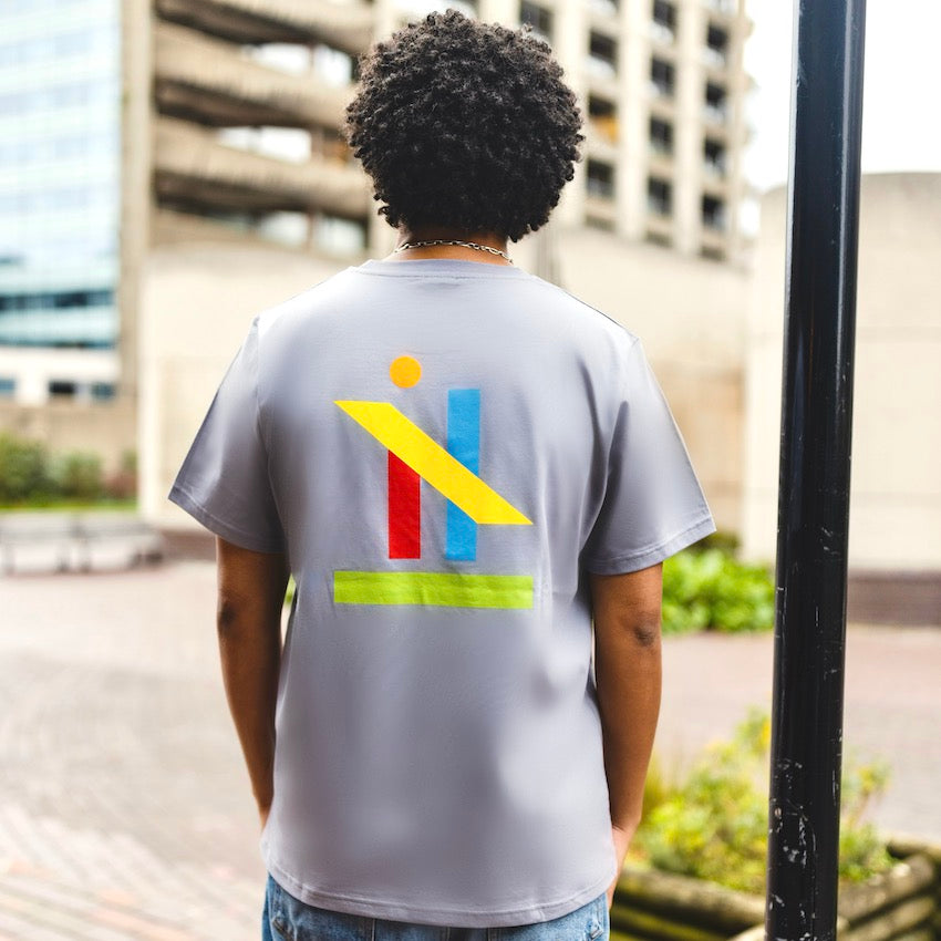 h clothing - male model with back to camera wearing pastel grey tshirt with graphic of colourful geometric shapes on back