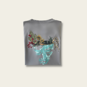 h clothing - flat shot of back of folded pastel grey tshirt with graphic of a face and a garden on top of the head