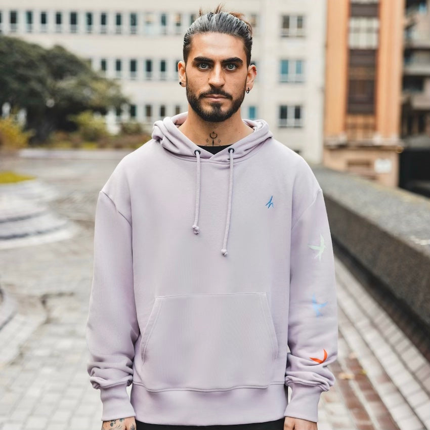 h clothing - male model facing the camera wearing light purple hoodie with colourful birds on left arm
