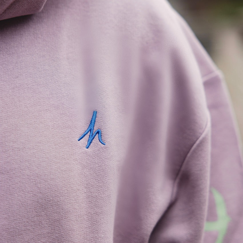 h clothing - close up of model wearing light purple hoodie with blue h logo on left breast