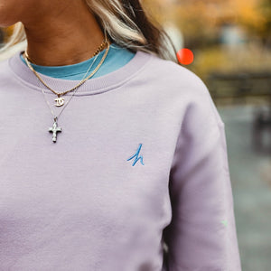 h clothing - close up of female model wearing light purple sweatshirt with blue h logo on left breast