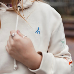 h clothing - close up of female model wearing off white cream hoodie with blue h logo on left breast