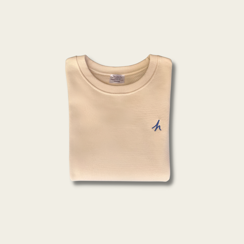 h clothing - flat shot of front of folded off-white sweatshirt with blue h logo on left breast