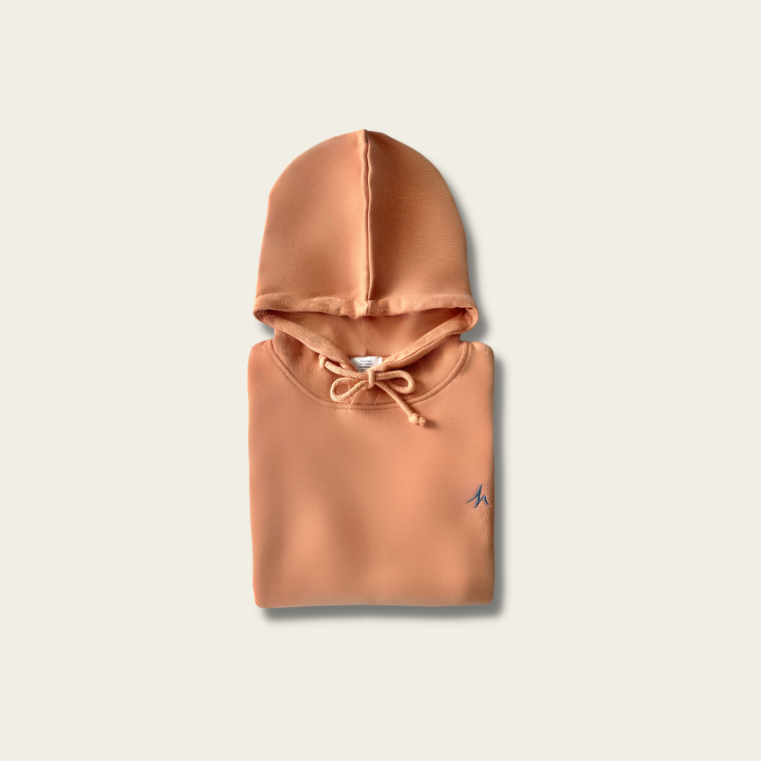 h clothing - flat shot of front of folded pastel orange hoodie with blue h logo on left breast