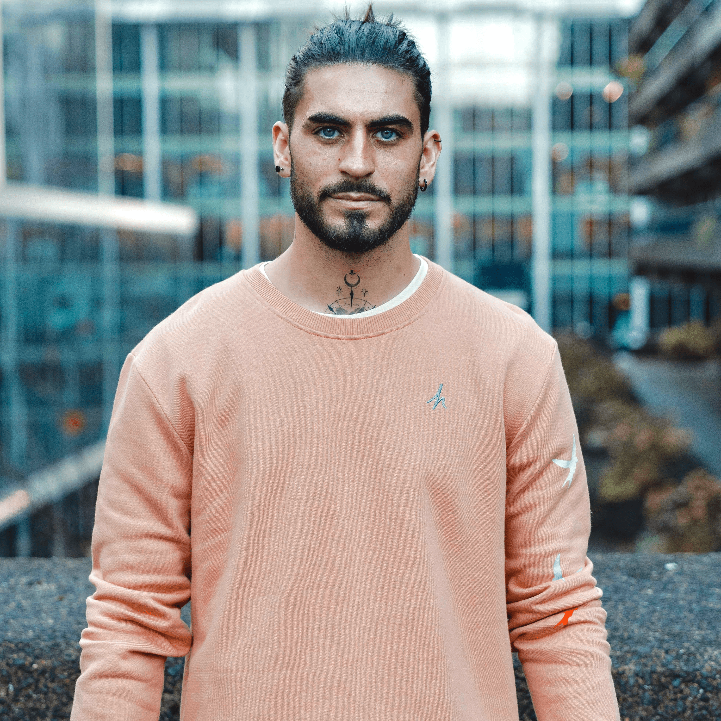 h clothing - male model facing the camera wearing pastel orange sweatshirt with blue h logo and colourful birds going down left arm