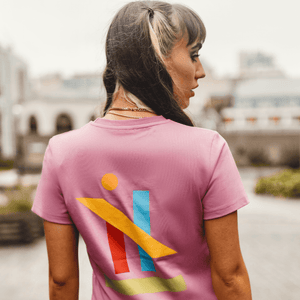 h clothing - female model with back to camera wearing a pastel pink tshirt with graphic of colourful geometric shapes