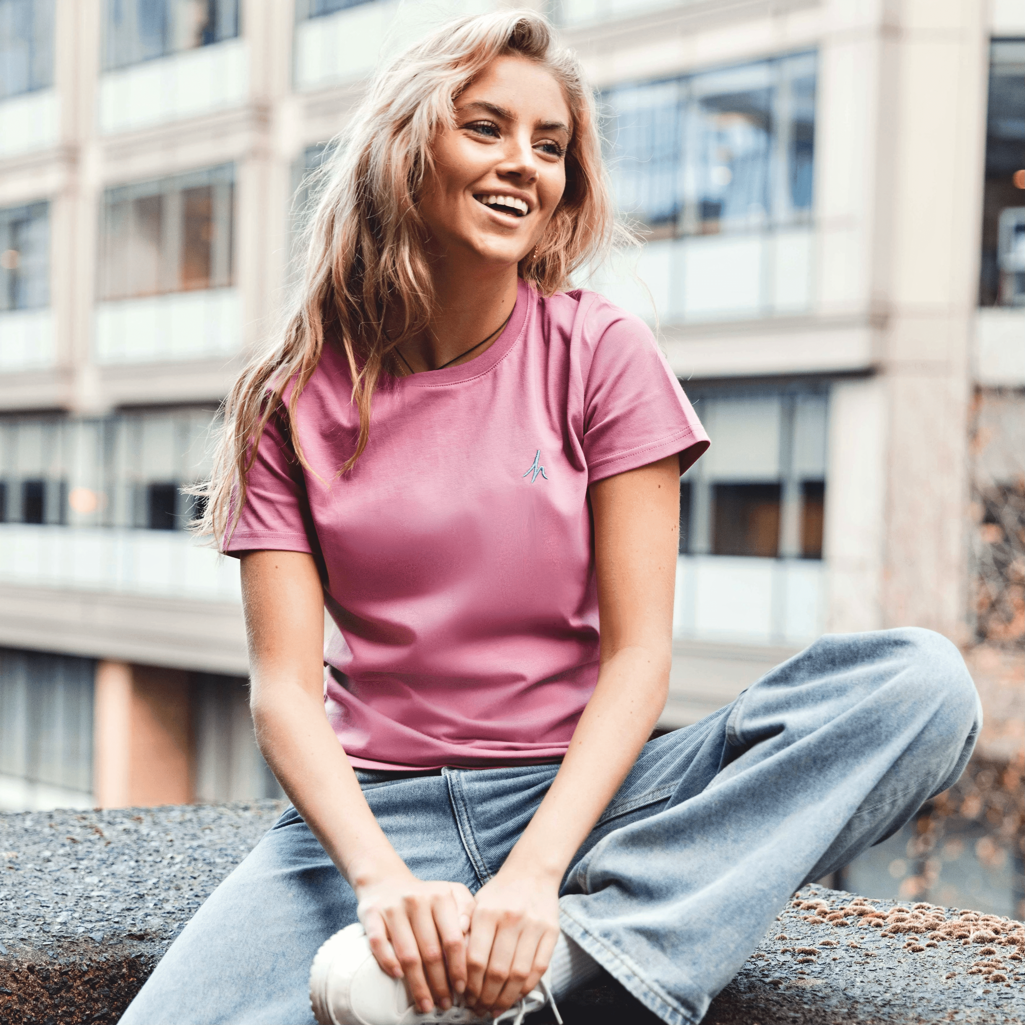 h clothing - female model sitting on ledge wearing pastel pink tshirt with blue h logo