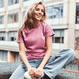 h clothing - female model sitting on ledge wearing a pastel pink tshirt with blue h logo