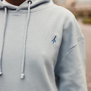 h clothing - close up of  model wearing sky blue hoodie with blue h logo on left breast