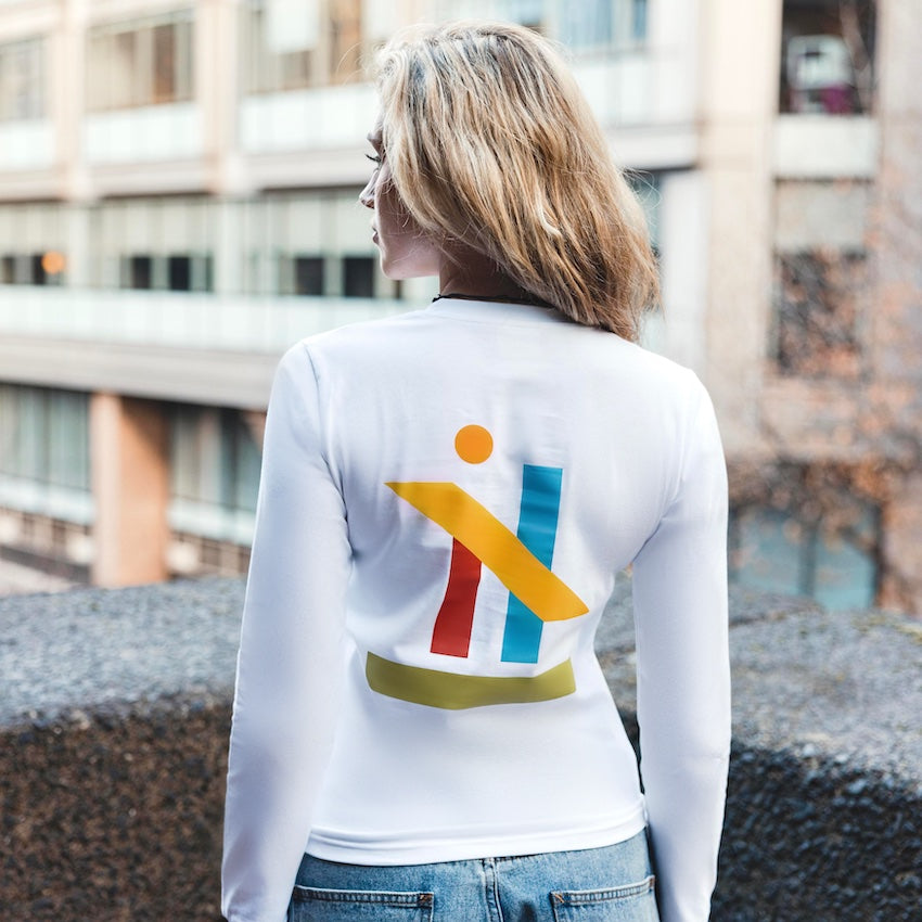 h clothing - female model with back to camera wearing white long sleeved tshirt with graphic of colourful geometric shapes