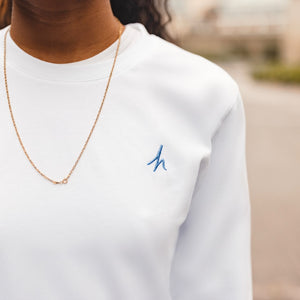 h clothing - close up of female model wearing white long sleeved tshirt with blue h logo on left breast