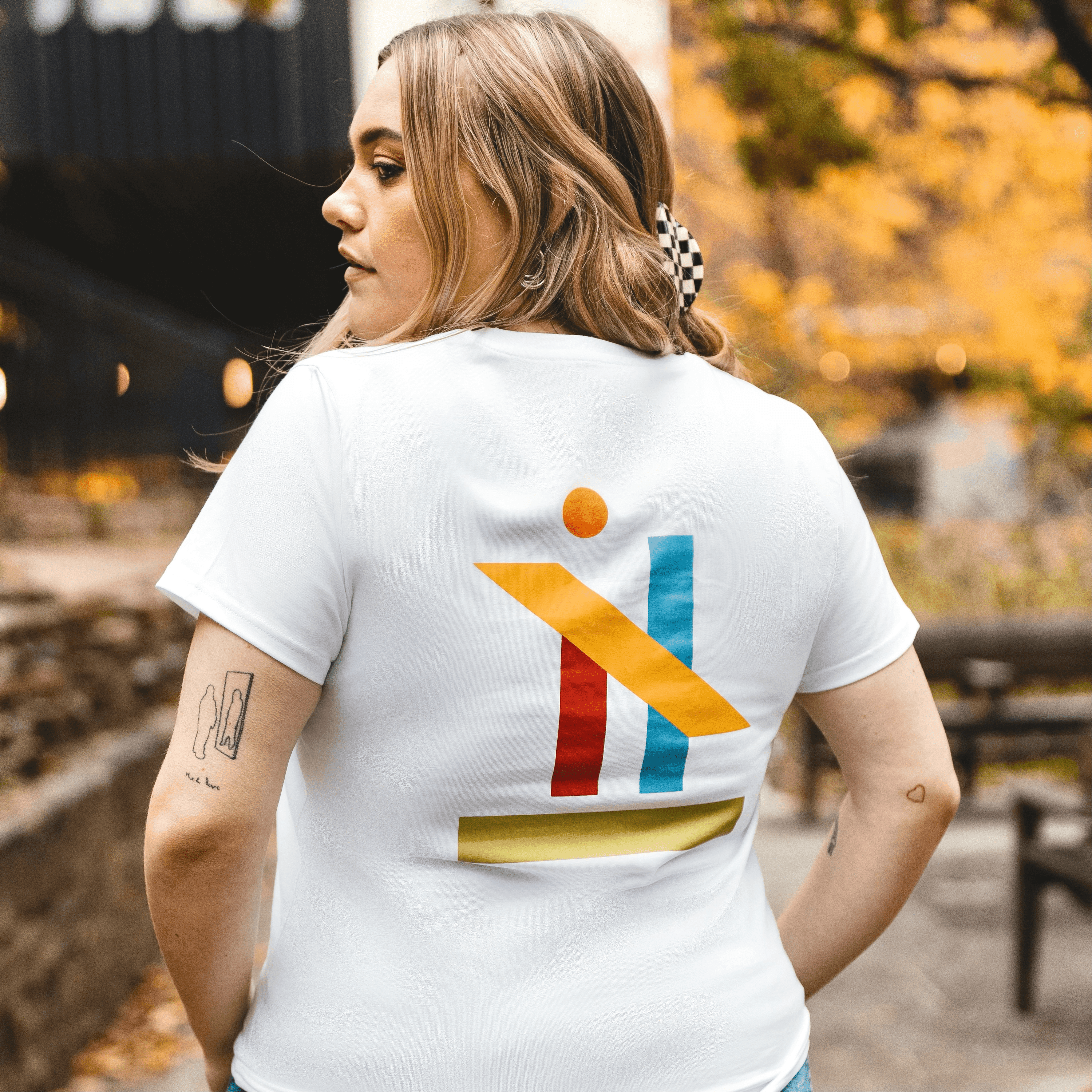 h clothing - female model with back to camera wearing white tshirt with graphic of colourful geometric shapes